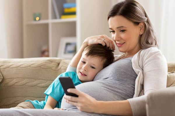 Gravid mamma med barn tittar på mobil